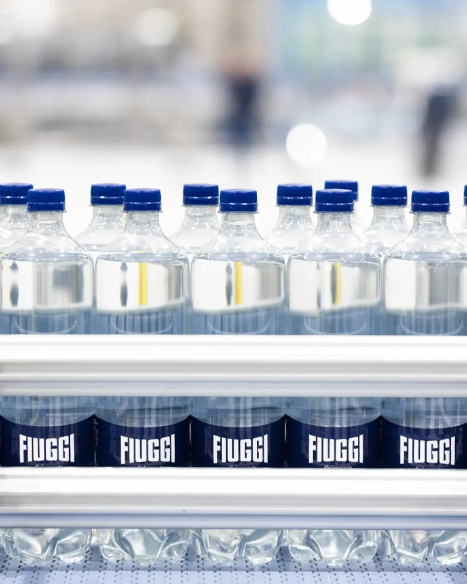 Acqua Fiuggi sparkling water bottles with blue caps arranged on shelves of a production line